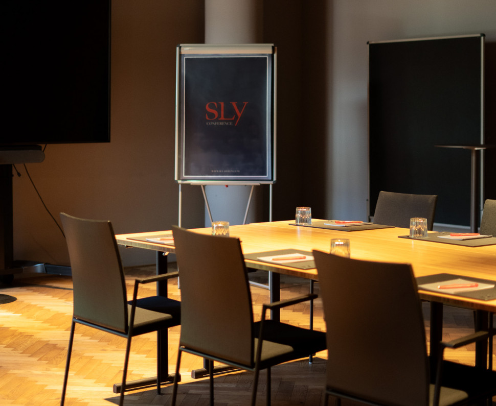 Ein Besprechungsraum im sly Hotel mit einem Konferenztisch mit Stühlen und einer Flipchart im Hintergrund.