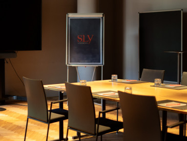 Ein Besprechungsraum im sly Hotel mit einem Konferenztisch mit Stühlen und einer Flipchart im Hintergrund.