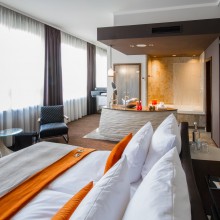 Blick über das Bett auf das offene Badezimmer in hellem Hotelzimmer