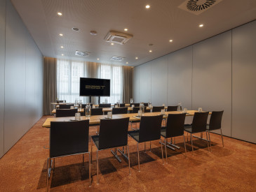 Moderner Konferenzraum mit Stuhlreihen und Tischen vor einer Präsentationsleinwand, bereit für ein Meeting oder Seminar.