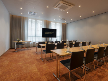 Modern conference room with rows of tables and chairs facing a large screen, set up for a meeting with water bottles and notepads.