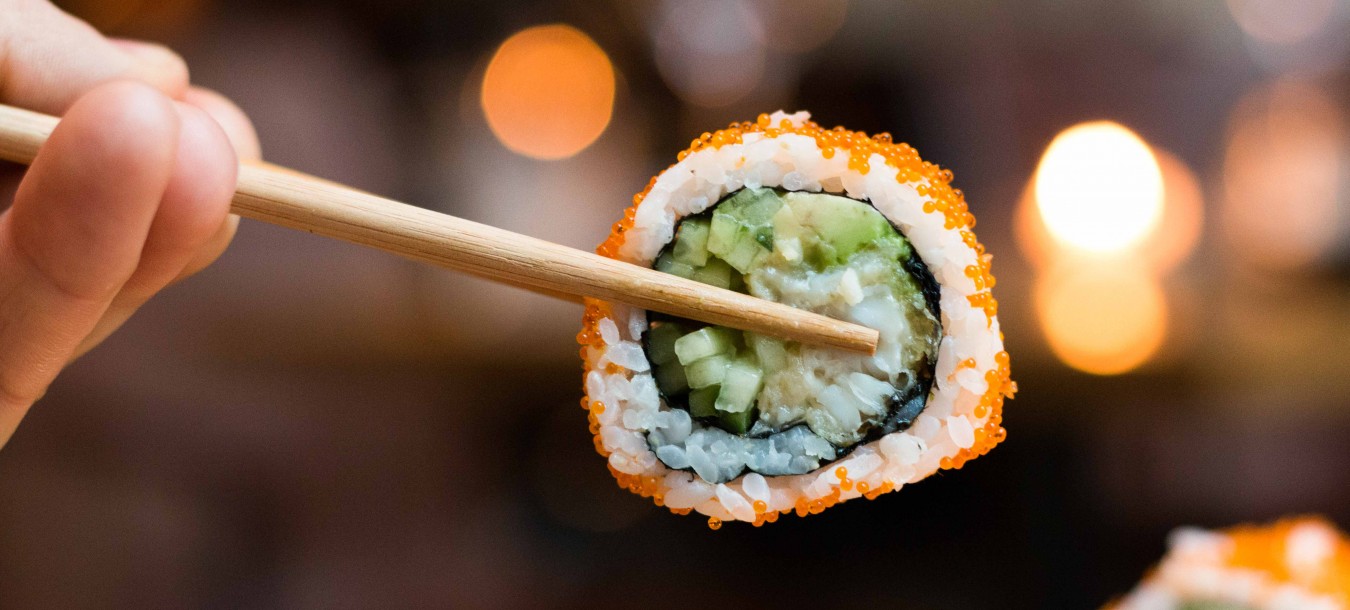 Hand holds sushi roll with wooden sticks
