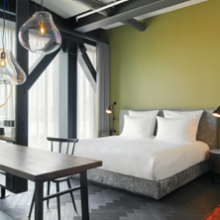Loft hotel room with green wall, hotel bed, table, chair and hanging lamps